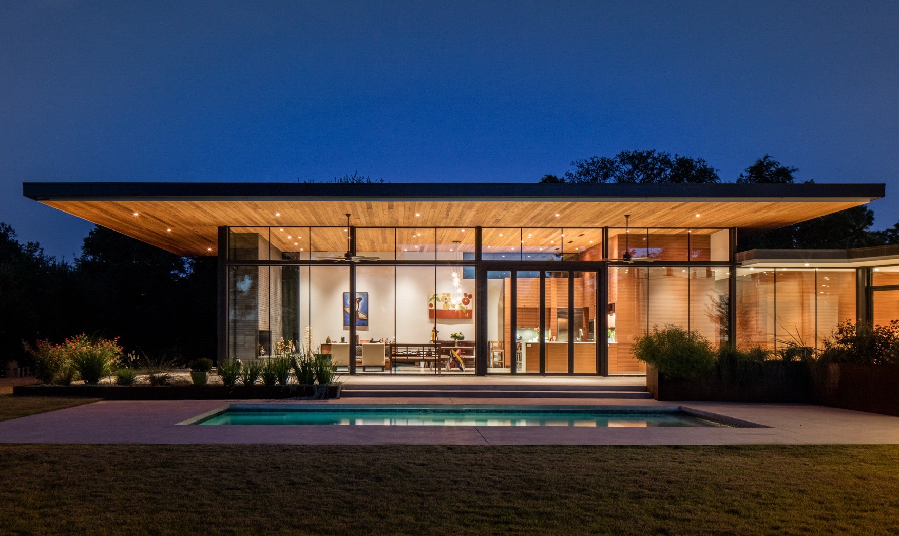 Residential architecture of a modern glass house with an in-ground pool outside.